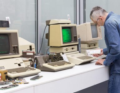 A man works at a computer. The man is wearing a blue lab coat.